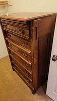 Angled view showing six drawer fronts with brass handles, dark wood finish, and the overall shape and height of the dresser.