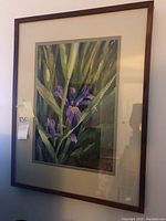 Frontal photo of framed watercolor painting of blooming purple iris flowers with natural lighting.