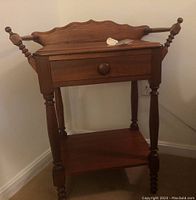 Front view of the solid wood side table showing single drawer, turned legs, wooden rail sides, and decorative backsplash back piece.