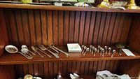 Wide view of shelf showing all silverplate utensils including spoons and asparagus server