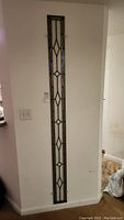 Full-length view of narrow rectangular stained glass panel hung on wall