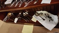 Overview of assorted sterling silver serveware including spoons, ladle, corn holders laid on shelf and cloth