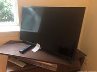 Samsung 32-inch TV shown with remote on top of a dark wooden surface. Zenith DVD/VCR player under the TV.