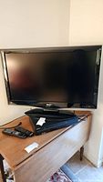 Front view of Sharp 42 inch TV on stand with Sony VHS/DVD player and remotes on a wooden desk.