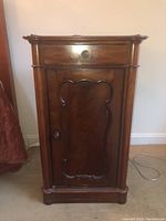Front view of the solid wood side table showing drawer and carved cabinet door with ornate wood panel.
