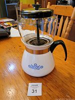 Two-piece Corning Ware coffee pot with glass percolator on top, black lid and handle, and white base pot with blue floral design and black handle.