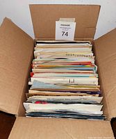 Box of over 100 45 RPM vinyl records viewed from above showing record sleeves stacked vertically.