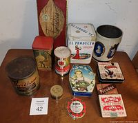 Top-down view of 12 assorted vintage tins on wooden surface showing variety in shapes, sizes, and designs including cigar and promotional tins.