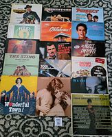 Photo showing 16 soundtrack and Broadway musical vinyl LP records arranged on carpeted floor. Titles visible include Westworld, Rhinestone, The Sting, Oklahoma, Hair, Flamingo Kid, and others.