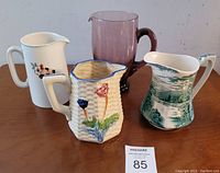 Four pitchers arranged on wooden surface showing shapes, colors and decoration