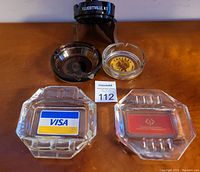 Front view of all five ashtrays showing issuer logos and overall condition