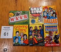 Front view of the six unopened wax packs featuring TV show titles M*A*S*H, Growing Pains, The A-Team, Dallas, The Gong Show, and American Gladiators.