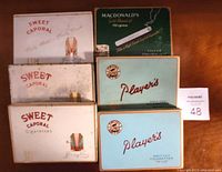 Photo showing 8 vintage smoker's tins including Player's, Sweet Caporal and MacDonald's brands, arranged for sale.