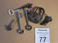 Photo of one old metal padlock with shackle and five vintage metal keys on neutral background, showing wear and patina.