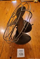 Side angled view of vintage Robbins & Myers desk fan showing metal blades, protective wire cage, and rounded base on wooden table.