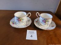 Two Royal Albert tea cups and saucers displayed on a wooden surface showing the floral pattern and gold trim.