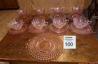 Full set of 17 pink Depression glass pieces including cups, saucers, dessert plates, bowls and cake plate arranged on wood table with auction tag.