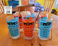Front view of 6 bingo glasses in wire carrier with orange and blue bingo card designs visible