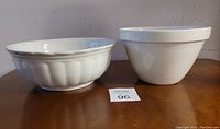 Two white vintage mixing bowls side by side, one with fluted design and one plain, showing overall condition and size comparison