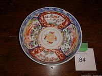Top-down view of very old Japanese bowl showing inner colorful floral and bird hand-painted designs with scalloped rim and central peach flower motif. Signs of chips and wear on rim visible.