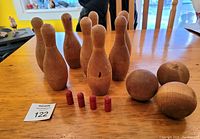 Front and top view of the skittles set showing 8 wooden pins, 3 wooden balls, and 4 red scoring pieces arranged on wooden table.