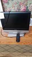 Front view of a 17 inch Trutech TV with remote placed in front of it on a wooden surface.