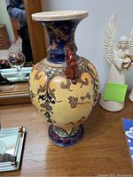 Full view of the ceramic vase showing intricate floral and ornamental patterns with a glossy finish and a small red sculpted detail on the body.