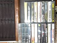 Brown carrying case for cassette tapes with soft padded compartments. Assortment of cassette tapes inside showing artist labels and titles.