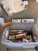 Plastic tub filled with multiple boxed Tyco train cars and locomotives along with track sections in plastic bags and power pack cords.