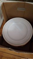 Photo showing stacked dinner plates with gold rim in a cardboard box.