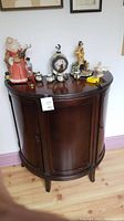 Front view of dark wood curved two-door wall cabinet with assorted decorative figures on top.