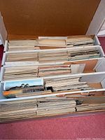 Cardboard box with rows of vintage postcards in dividers; labels visible