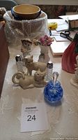 Photo showing Lenox cat salt and pepper shakers, porcelain figurines, vase with flowers, and blue swirl glass perfume bottle on a white textured tablecloth.