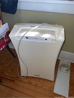 Full view of white portable air conditioner with power cord and plastic vent panel on floor