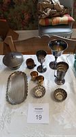 Full view of all silverplated items on white cloth including covered dish, goblets, small cups, scalloped bowls, tray, and tumbler