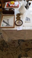 Full lot photo showing ceramic vase, framed Verrazano Bridge art with stamp, coasters, small round framed art, unframed black and white sketch, wooden double spool container.
