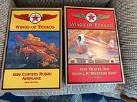 Two boxed Wings of Texaco collectible airplane models side by side on a fabric surface.
