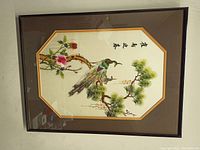 Framed silk embroidery artwork showing the full piece in the frame, with a bird on a branch and script characters