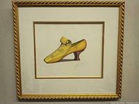 Framed fancy shoe print, showing full artwork and frame, featuring a yellow vintage shoe with curled top and dark heel, signed.
