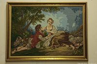 Full view of framed needlepoint showing two figures reclining outdoors with sheep and trees