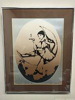 Framed artwork of Pierrot figure holding a candle, seated on crescent moon with floral silhouettes, signed and dated at the bottom.
