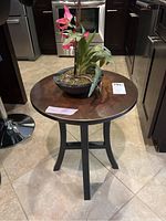 Table with copper-toned round top and faux flower plant on top, showing full height and surroundings.