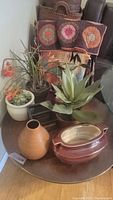 Photo of faux plants in various ceramic pots on a round table with colorful woven textiles in the background
