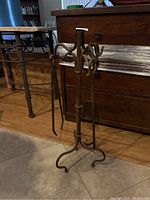Metal fireplace accessory set includes poker, shovel, prong tongs hung on a metal stand with curved legs and hooks.