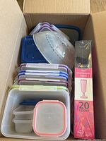 Box containing stacked plastic food storage containers with lids in various colors and a microwave splatter cover