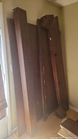 Disassembled wooden king size bed frame pieces stacked against wall: headboard, footboard, and side rails.