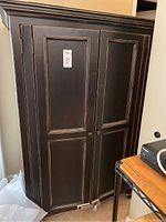 Front view of the black distressed wooden armoire with paneled doors and round knobs.