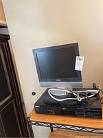 Samsung monitor with a silver bezel and round base stand with cables coiled on top of a Panasonic DVD player.