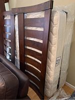 Photo showing the footboard and mattress wrapped in plastic, with dark wood horizontal slats curved outward.
