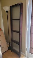 Single folded panel of room divider leaning against a wall next to floor lamp.
